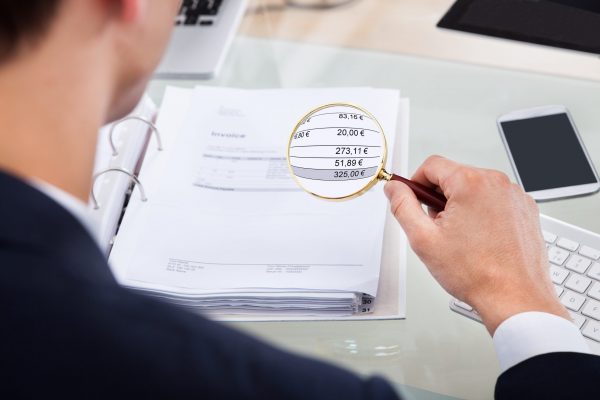 Cropped image of auditor examining invoice with magnifying glass at desk